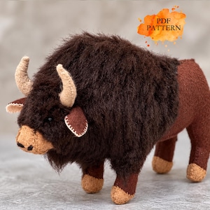 May include: A plush bison toy featuring dark brown faux fur on the head and shoulders, a tan muzzle, and light beige horns. The body is made of smooth brown fabric with tan lower legs. An orange watercolour graphic displays the text PDF PATTERN.