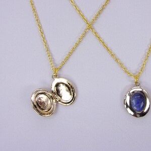 May include: Two gold chain necklaces with oval-shaped lockets. One locket is open and has a plain interior. The other locket has a blue stone inside.