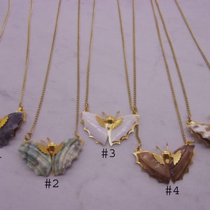 May include: Five gold chain necklaces with butterfly pendants made from different types of seashells. The butterflies are all different colors and patterns. The necklaces are numbered 1 through 5.