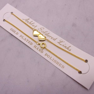 May include: Gold-plated anklet with two heart charms. The delicate chain is attached to a clasp. The card reads "Anklet Soldered Links Gold Plated Hand Polished."