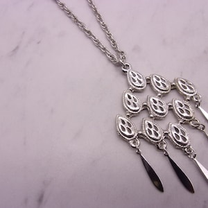 May include: Silver-toned necklace with a cascading pendant. The pendant features three tiers of openwork teardrop shapes, each with a central design. Elongated, slender dangles hang from the bottom tier. The chain is a simple, twisted design.