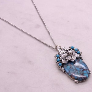 May include: A silver chain necklace with a turquoise and silver pendant featuring a rose design. The pendant is surrounded by turquoise stones.