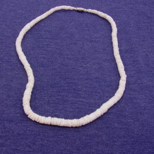 May include: A white shell necklace made of small, round, flat shells. The necklace is strung on a thin cord and has a silver clasp.