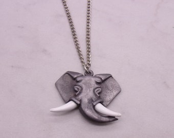 May include: A silver chain necklace with a pewter elephant pendant. The elephant has white tusks and a detailed design.