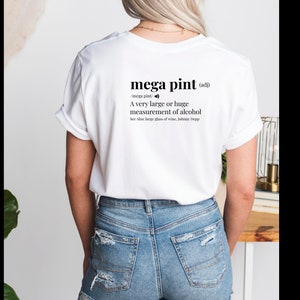 以下が含まれることがあります： 「メガピント（形容詞）」と黒文字で書かれた白いTシャツ。単語は「非常に大きく、または巨大なアルコールの測定値」と定義されています。