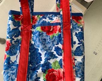Könnte beinhalten: Eine rote und blaue Blumentasche mit roten Tragegurten. Die Tasche hat einen weißen Hintergrund mit blauen und roten Blumen.