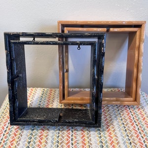May include: Two wooden picture frames, one black and one brown, with a simple design. The frames are stacked on top of each other.