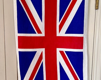 May include: A white tea towel with a red, white, and blue Union Jack design. The tea towel is made of 100% cotton and says "Made in USA" in the bottom corner.