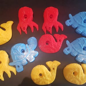 May include: A set of nine colorful plastic climbing holds shaped like sea creatures. The holds are in various shades of blue, yellow, and red. They are designed for indoor climbing walls.