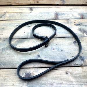 Puede incluir: Una correa de perro de cuero negro con un cierre de metal.