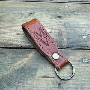 May include: A brown leather keychain with a metal ring and a stitched design. The keychain has the letter "M" embossed on it.