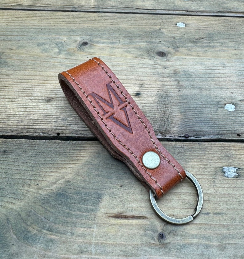 May include: A brown leather keychain with a metal ring and a stitched design. The keychain has the letter "M" embossed on it.