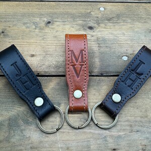 May include: Three leather keychains with metal rings. The keychains are brown, black, and dark brown. Each keychain has a different set of initials embossed on the leather. The initials are "JH", "MV", and "JH".