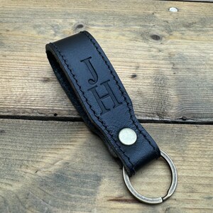 May include: Black leather keychain with a brass key ring. The keychain has the initials "JH" embossed on it.