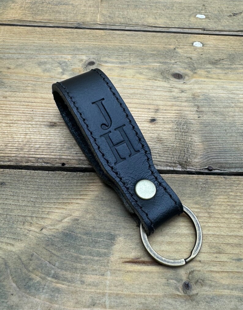 May include: Black leather keychain with a brass key ring. The keychain has the initials "JH" embossed on it.