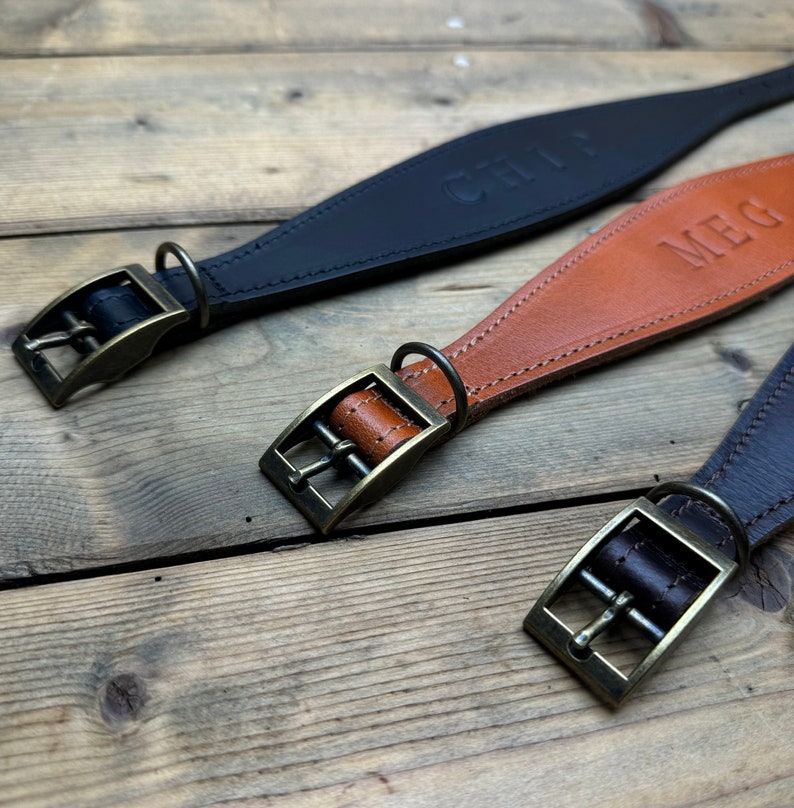 May include: Three leather dog collars with brass buckles. The collars are brown, black, and brown. The collars are personalized with the names "Meg", "Chili", and "Meg".