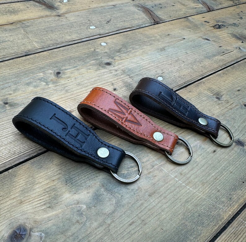 May include: Three leather keychains with metal rings. The keychains are brown, black, and tan. Each keychain has a different set of initials embossed on the leather.