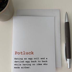 Peut inclure: Carte de vœux blanche avec le mot "Potluck" en marron. Le texte décrit avec humour l'expérience d'un potluck. Un stylo et une petite plante en pot sont à côté de la carte.