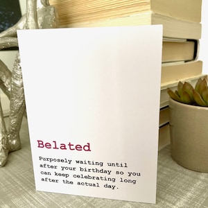 May include: A white card with the word "Belated" in pink lettering. The card defines "Belated" as "Purposely waiting until after your birthday so you can keep celebrating long after the actual day."