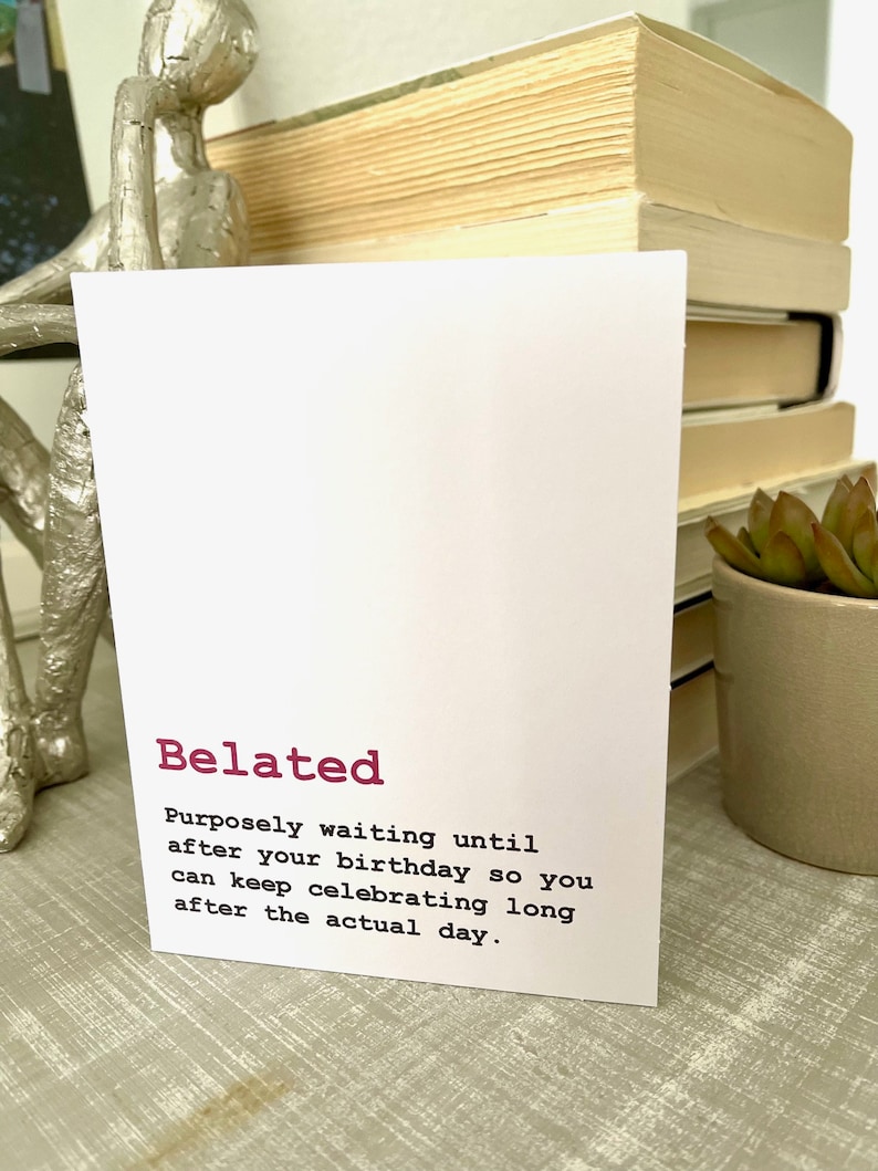 May include: A white card with the word "Belated" in pink lettering. The card defines "Belated" as "Purposely waiting until after your birthday so you can keep celebrating long after the actual day."