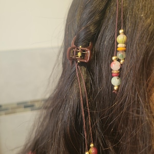 May include: A brown hair clip with a beaded string attached. The beads are multi-colored and include green, red, orange, and white.