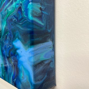 May include: Close-up of the side of a canvas painting with blue, green, and black abstract swirls.