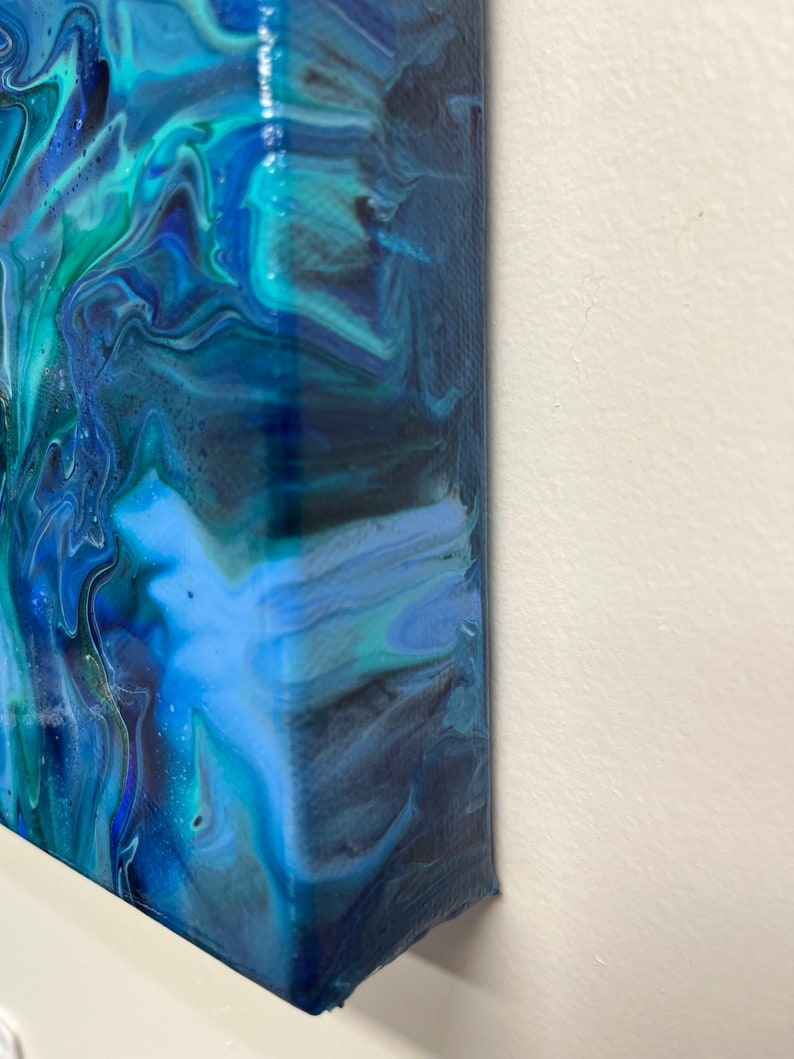 May include: Close-up of the side of a canvas painting with blue, green, and black abstract swirls.