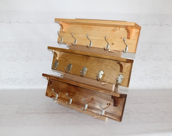 May include: Three wooden shelves with hooks, each shelf is a different shade of wood, the top shelf is light wood, the middle shelf is medium brown, and the bottom shelf is dark brown.