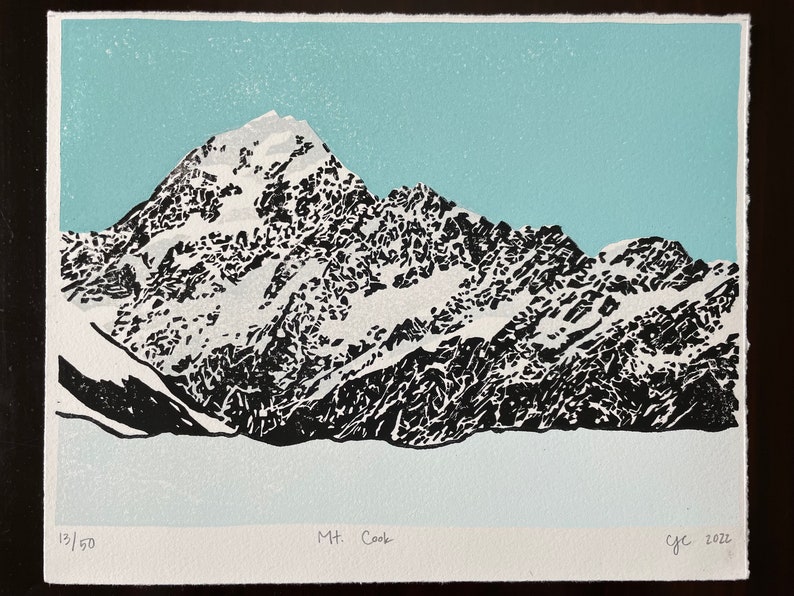 May include: A black and white woodcut print of Mount Cook, a snow-capped mountain range in New Zealand. The print is numbered 13/50 and signed "c.y.c. 2022".