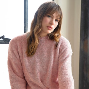 May include: A pink fuzzy sweater and shorts set. The sweater has long sleeves and a crew neck. The shorts have a drawstring waist.