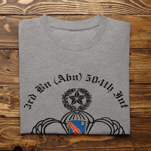 May include: A gray t-shirt with a black print of the 3rd Bn (Abn) 504th Inf. The print features a parachute, a star, and a wreath.