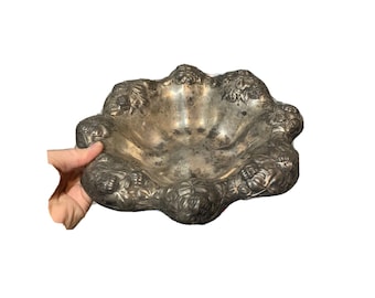 May include: A silver-toned metal bowl with a scalloped edge and a floral design. The bowl is made of a heavy metal and has a vintage look.