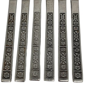 May include: Set of six silver-toned flatware pieces with a floral design. The handles are decorated with a repeating pattern of flowers and leaves.