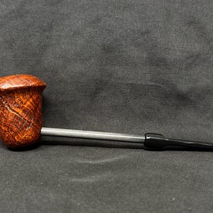 May include: A tobacco pipe with a rounded, textured, brown bowl and a silver stem. The mouthpiece is black. The pipe is set against a dark background.