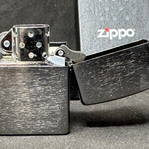 May include: A brushed metal Zippo lighter with the lid open, showing the inside. The lighter is rectangular with rounded edges and a textured surface. The Zippo logo is visible on the packaging in the background.