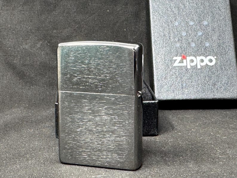 May include: A silver Zippo lighter with a brushed metal finish. The rectangular lighter has a textured surface. The Zippo logo is displayed on the box in the background.