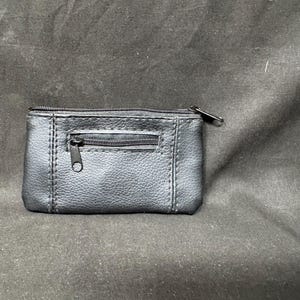 May include: A small, black leather coin purse with two zippered compartments. The purse has a rectangular shape with visible stitching and a textured surface. The zippers have metal pulls.