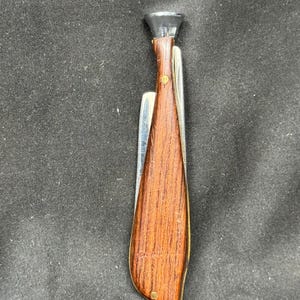 May include: A vintage pocket knife with a wooden handle and a silver blade. The handle is a rich brown color with brass accents. The knife has a black cap on the top. The blade is partially open.