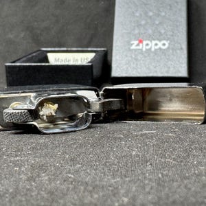 May include: Open chrome Zippo lighter with a black box in the background. The lighter is open, revealing the interior components. The box has the Zippo logo and the words "Made in US".