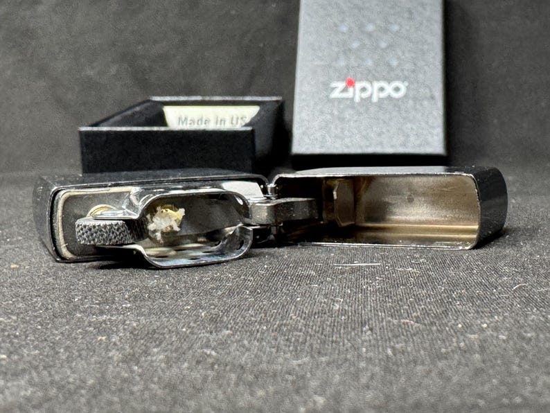 May include: Open chrome Zippo lighter with a black box in the background. The lighter is open, revealing the interior components. The box has the Zippo logo and the words "Made in US".
