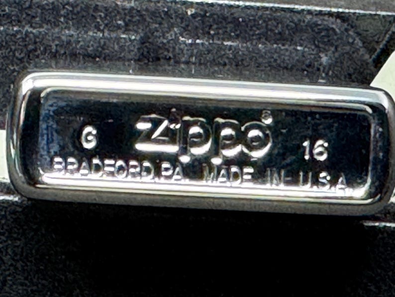 May include: A close-up of a chrome Zippo lighter. The lighter features the Zippo logo and the text "BRADFORD PA. MADE IN U.S.A." embossed on the surface. The number "16" is also visible.