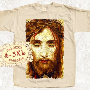 May include: A beige t-shirt with a mosaic image of Jesus Christ's face. The image is in shades of brown, gold, and red. The text "All Sizes S-5XL Available" is printed on a white lace circle.