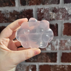 May include: A translucent pink soap bar with a unique, bubbly design. The soap is shaped like a flower with multiple rounded petals.