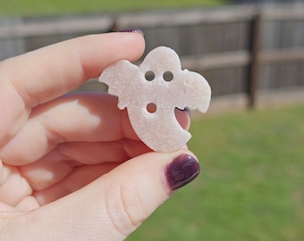 May include: A white ghost-shaped cookie with three holes for eyes and a mouth.