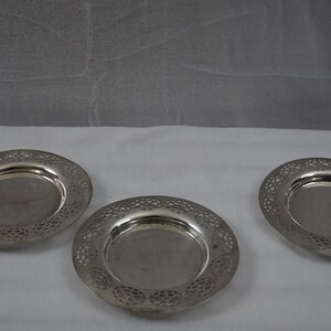 May include: Three silver-colored, round, decorative coasters with an intricate, openwork design.