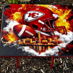May include: A red and black table featuring a football helmet and football with the Kansas City Chiefs logo. The design includes a cityscape and fiery background.