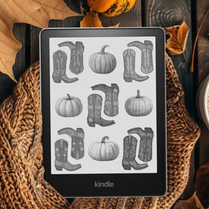 May include: A black and white Kindle e-reader displaying a digital image of a pattern of cowboy boots and pumpkins. The Kindle is on a brown knitted surface with fall leaves and a cup of coffee.