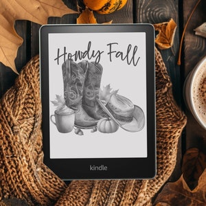 May include: A Kindle e-reader displaying a grayscale illustration with the text "Howdy Fall". The image features cowboy boots, a hat, a pumpkin, and a coffee mug. The e-reader is surrounded by a cozy brown knitted scarf, autumn leaves, and a cup of coffee.
