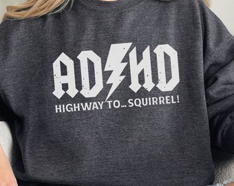 May include: A dark gray sweatshirt with a white graphic that says "ADHD HIGHWAY TO... SQUIRREL!" The graphic is in a rock and roll font with a lightning bolt.