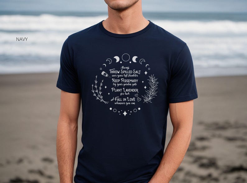 May include: Navy blue t-shirt with white text and illustrations. The text includes phrases like "Throw spilled salt" and "Plant lavender." The design features crescent moons, stars, and sprigs of herbs, creating a mystical theme.